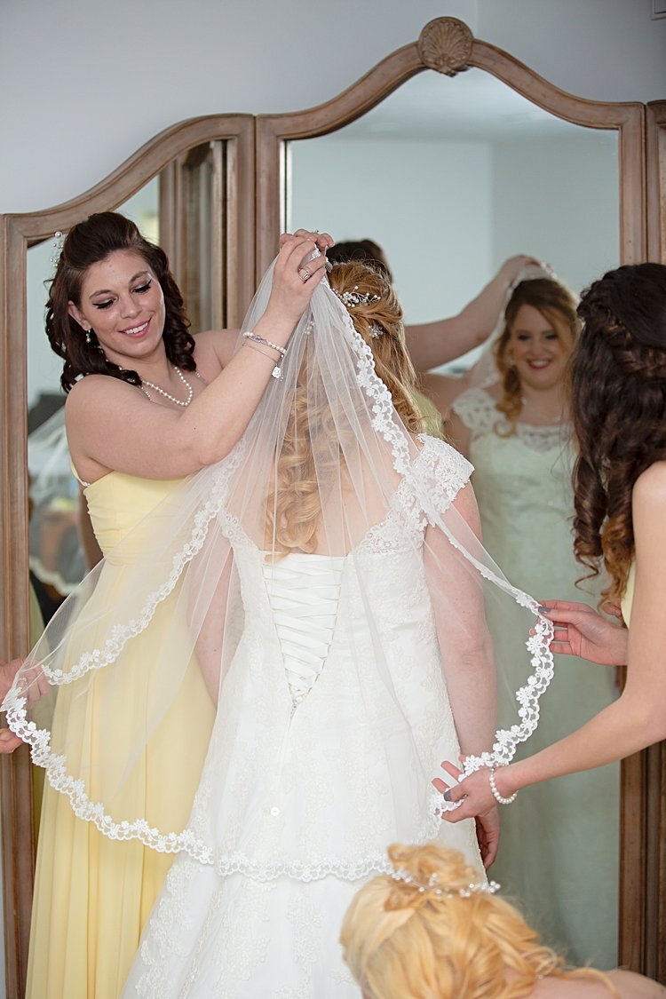 Bride standing in front of antique mirror while bridesmaids attach her veil