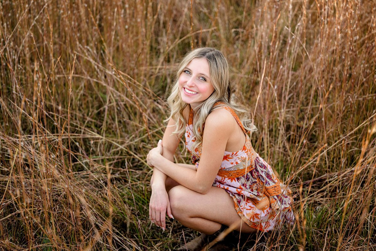 waxhaw senior bends down in tall grass during her portrait session