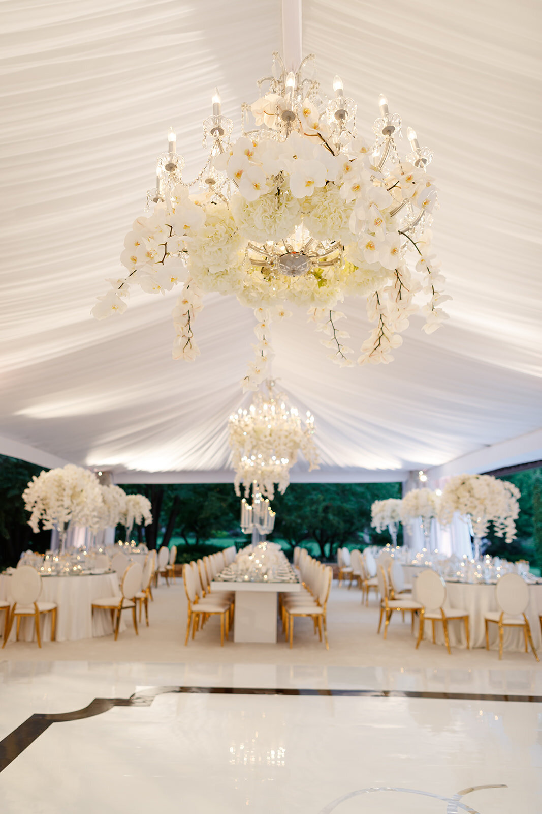 Wedding reception venue under a tent with opulent chandeliers and floral arrangements.