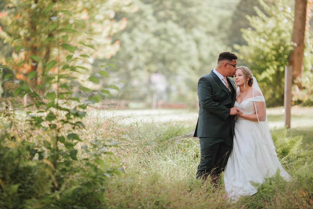 A bride and groom share an intimate moment in a serene, sunlit meadow.