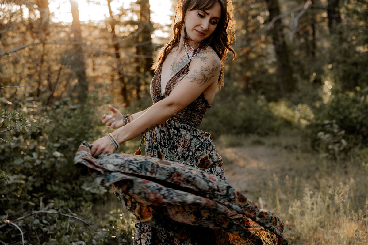 mom dancing in a flowy dress in a treed area with the sun peering through the trees