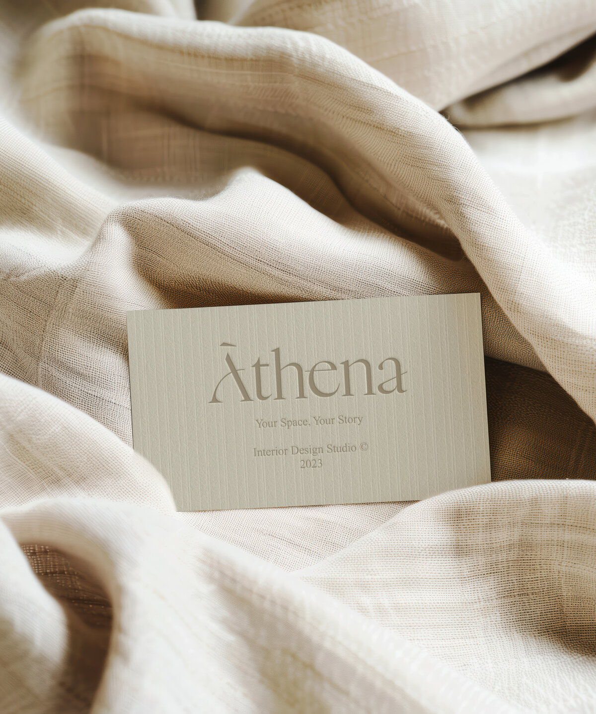 Athena brand identity with minimalist business card design for interior design studio, styled on neutral textured fabric.