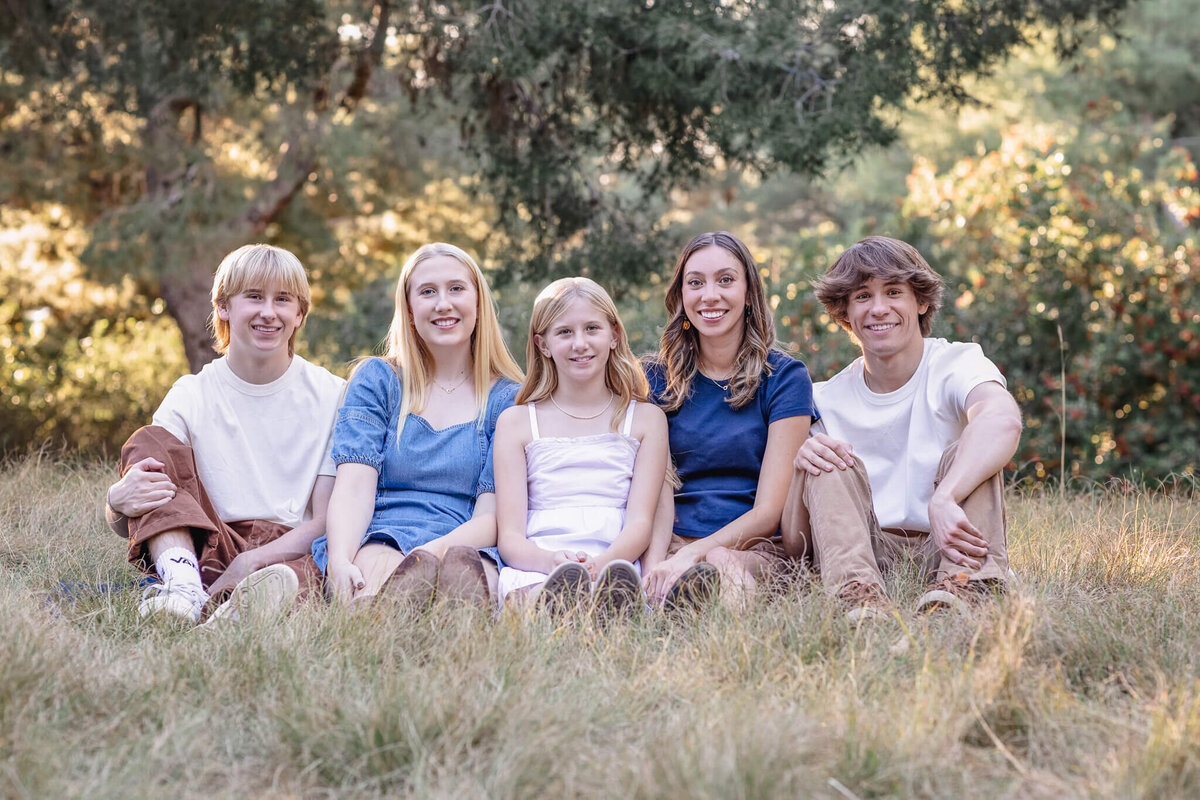 Five cousins sitting in the grass, smiling at the camera and wearing shades of blue and white at Jeffrey Open Space.