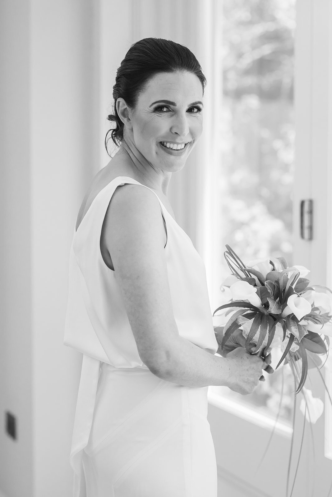 Black and white image of a bride holding her bouquet and smiling at the camera