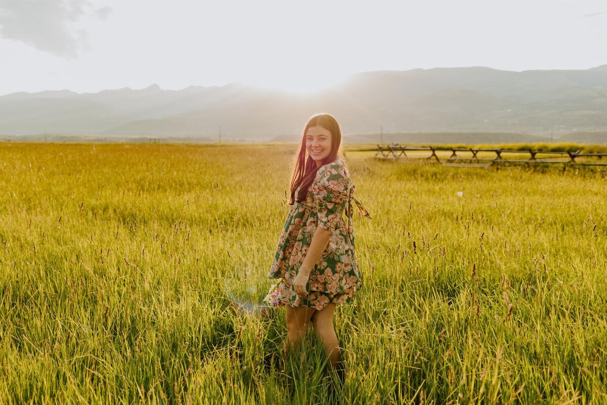 Senior poses in a field with mountains.