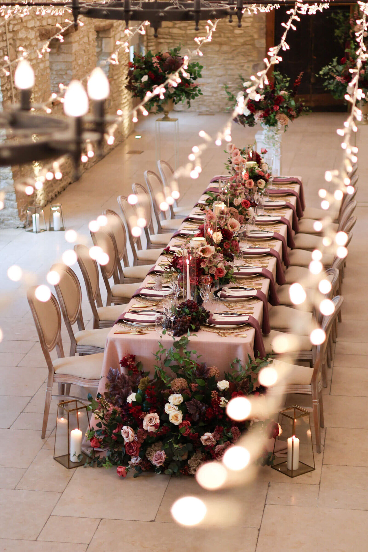 Cosy winter wedding table setting under fairy lights in the barn at Caswell House