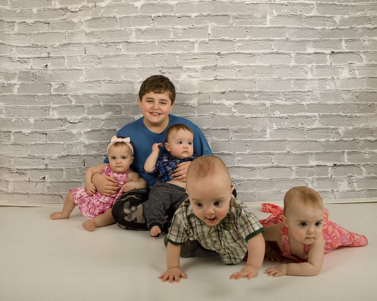 1 year old quadruplets posing with their big brother. 2 sitting by him and the other 2 trying to crawl away.