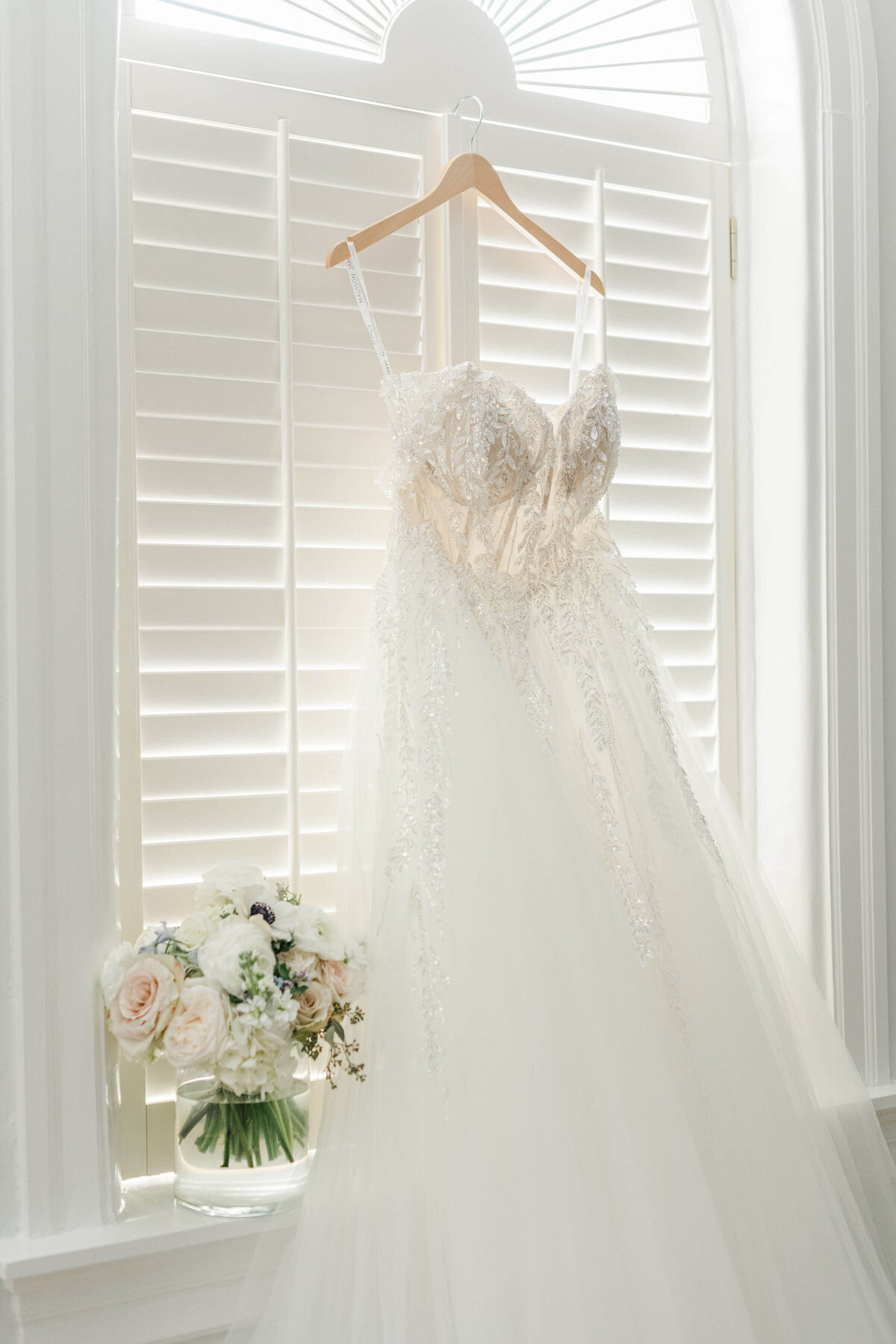 Bride dress hanging in window next to weedding bouquet