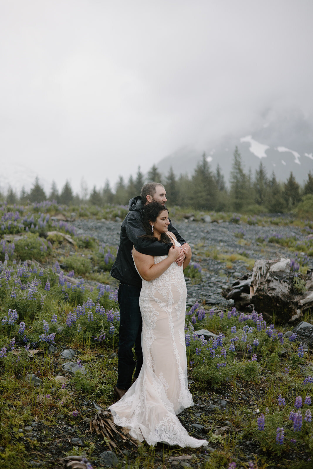 Elopement couple embraces in misty lupine field looking ahead.