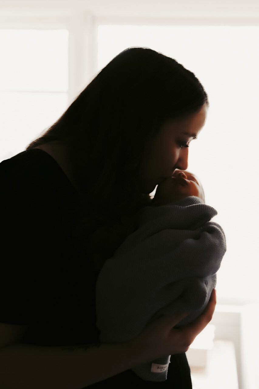 Beautiful lifestyle newborn photography in Tifton, GA: Silhouette of mother kissing newborn's nose