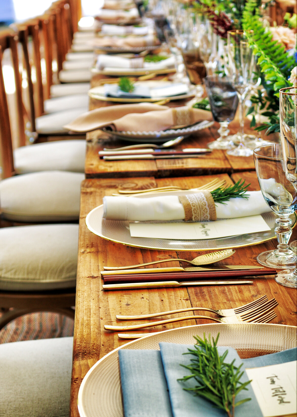 A rustic wooden table is laid for a wedding dinner or party with greenery creating a simple event decor.