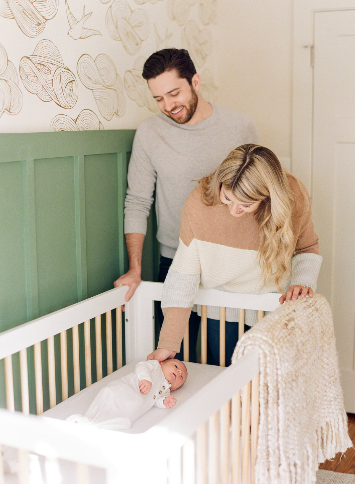 Mom and dad look lovingly over their new baby laying in the crib during a newborn photography session in Raleigh. Photo by Raleigh Newborn Photography A.J. Dunlap Photography.