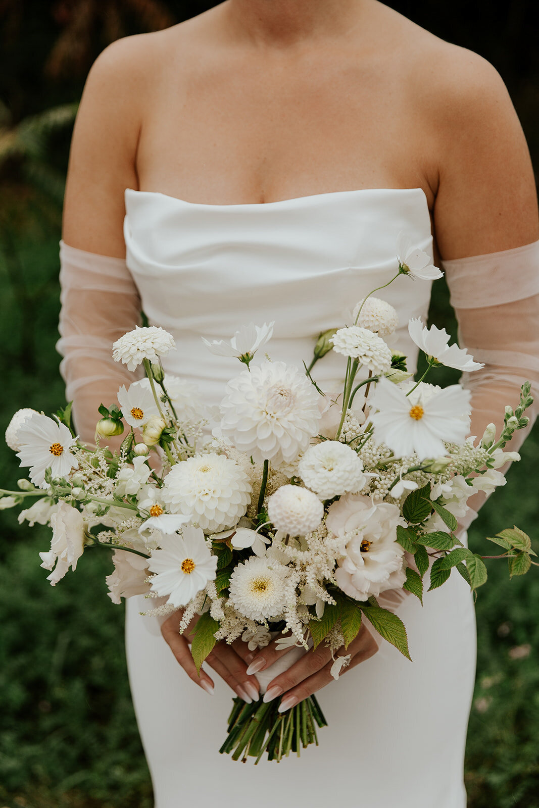 A bride holds a beautiful bouquet of white flowers in the garden at a Montreal wedding. 