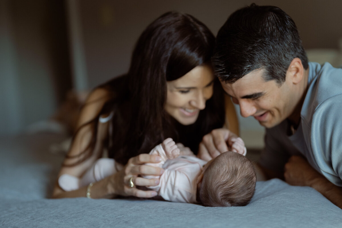 A heartfelt image of parents lying close together with their newborn, radiating warmth and joy as they share a moment of bonding and smiles. This candid and tender capture emphasizes the loving connection within the family.
