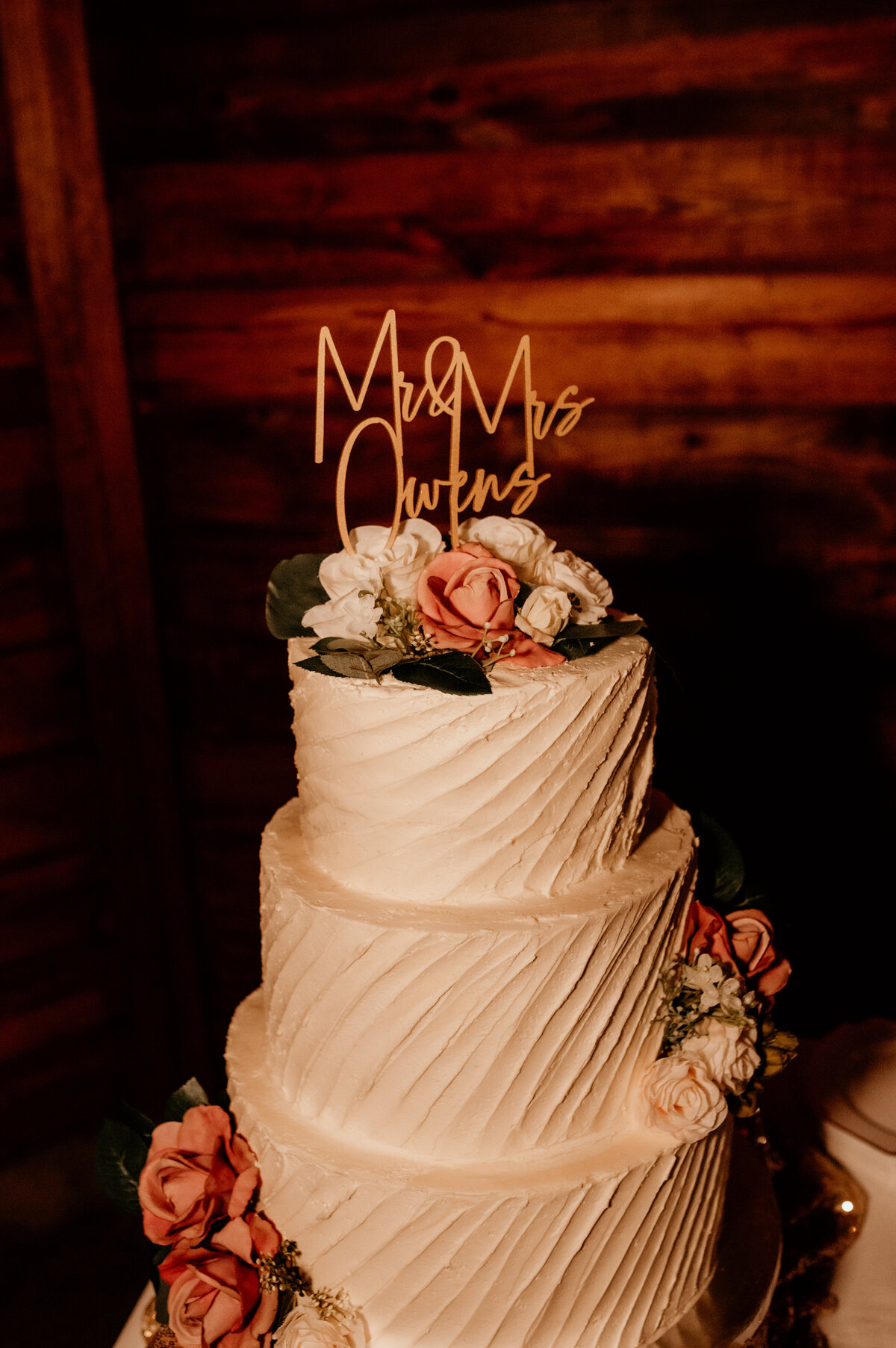 white buttercream wedding cake with three tiers is decorated with pink florals and a gold wedding cake topper