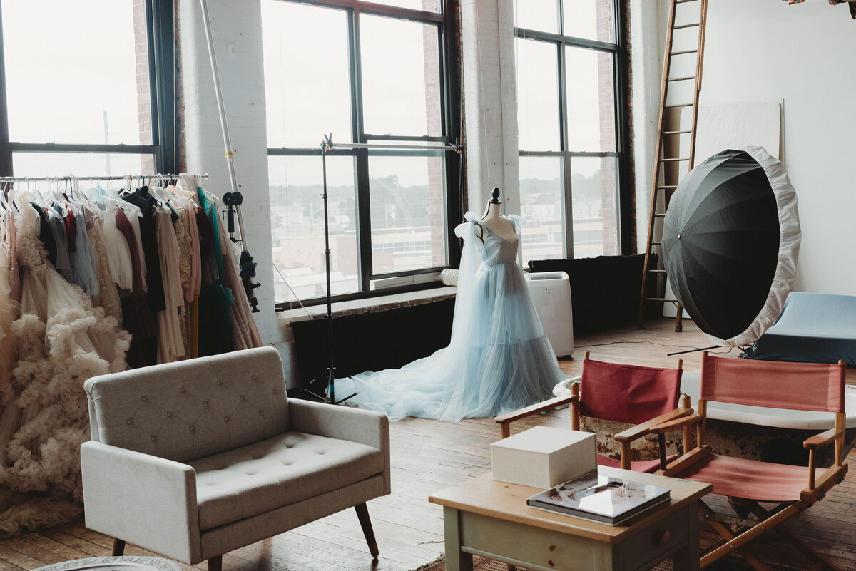Portrait studio with tall walls of windows, white walls and mannequin wearing soft blue gown