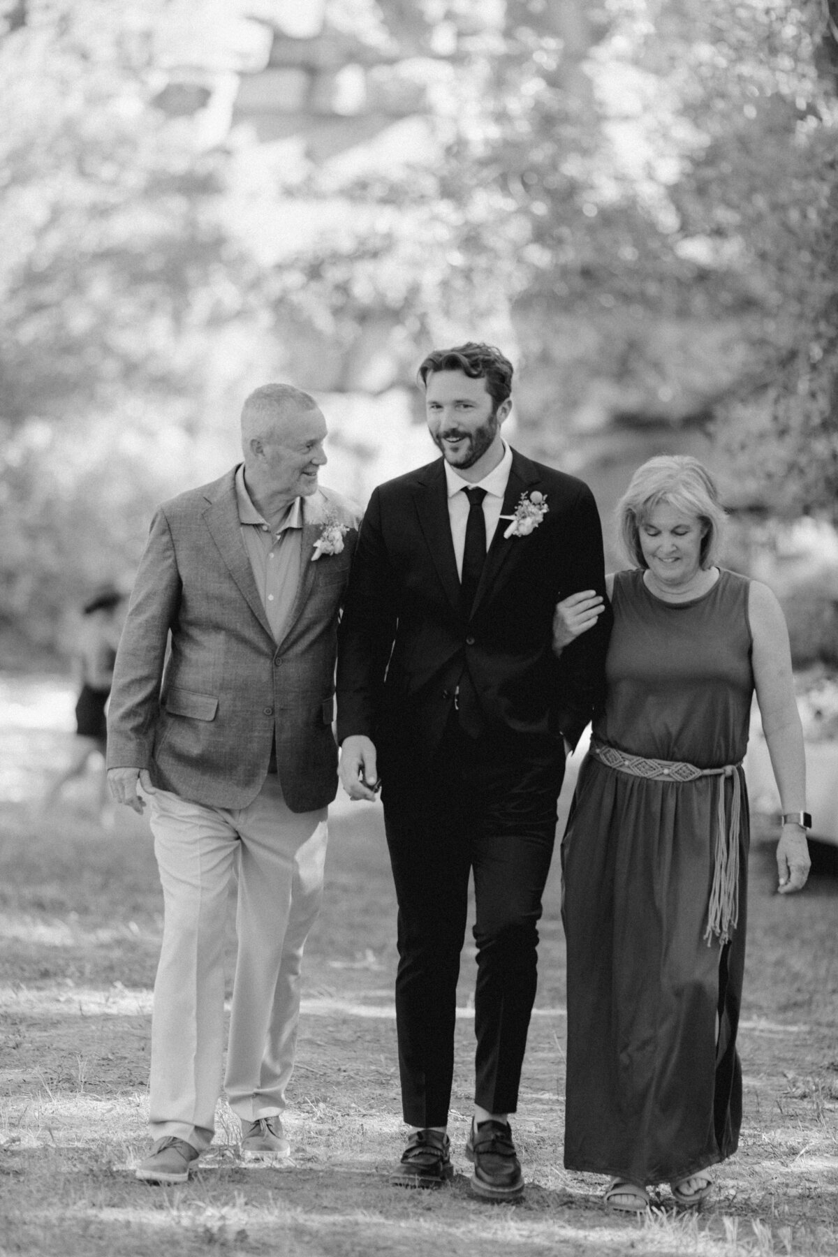 Groom walking along with parents on each arm