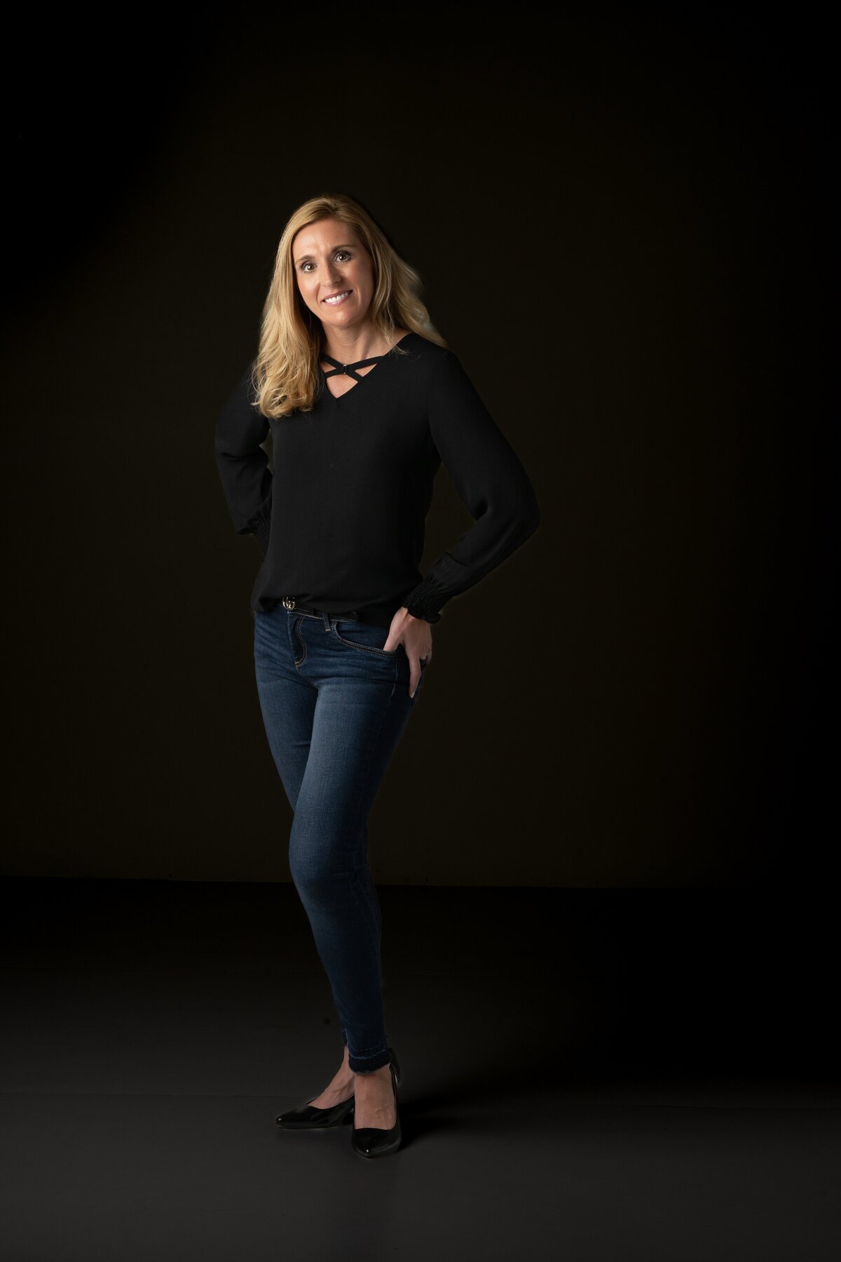 Women dressed in black shirt and dark jeans on black background for professional headshot