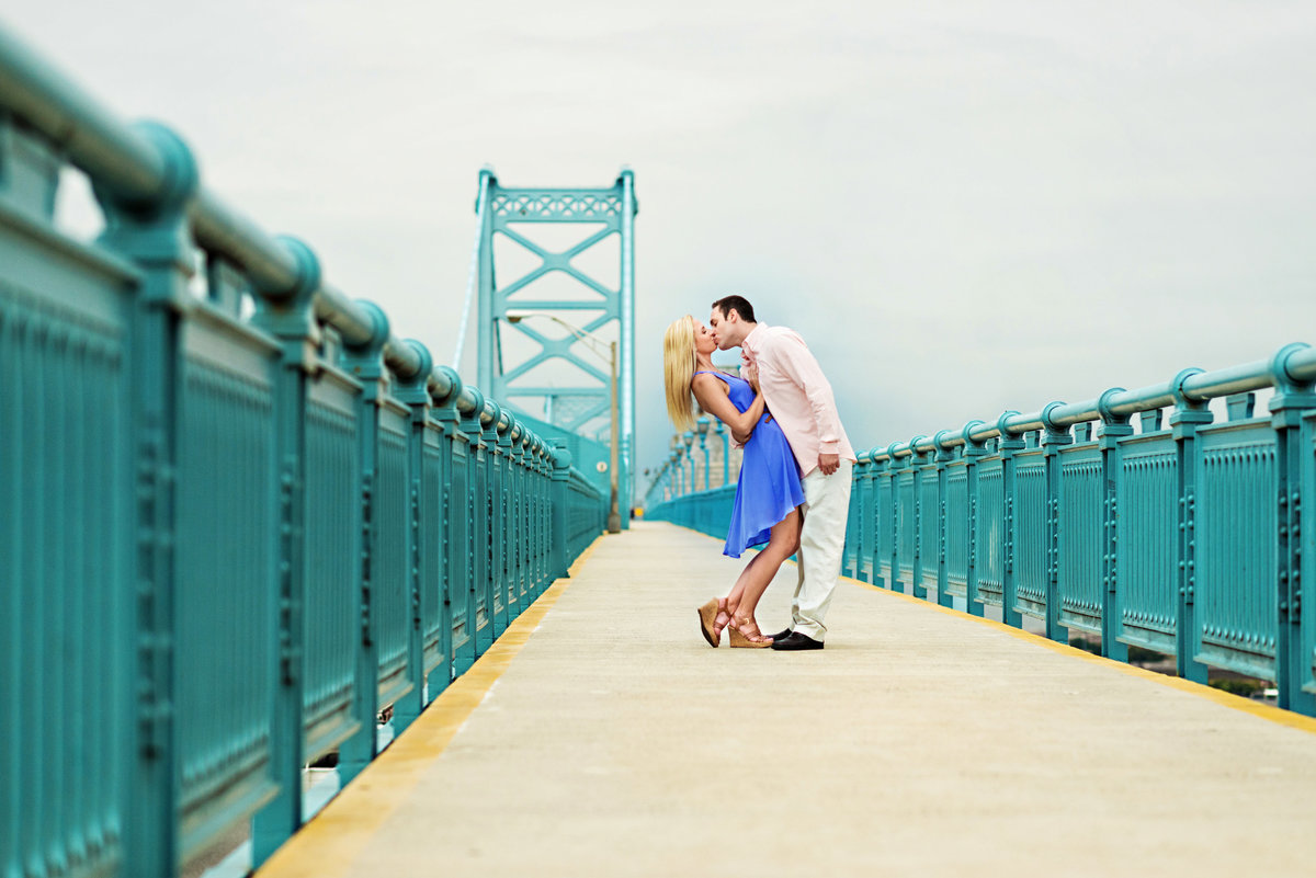 A couple kiss on top of the ben franklin bridge.