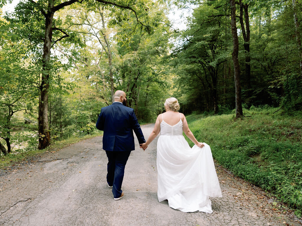 Bride and groom walking hand in hand down a quiet forest road in Greenbrier during their eloping to Gatlinburg celebration, surrounded by lush greenery and peaceful woodland scenery.
