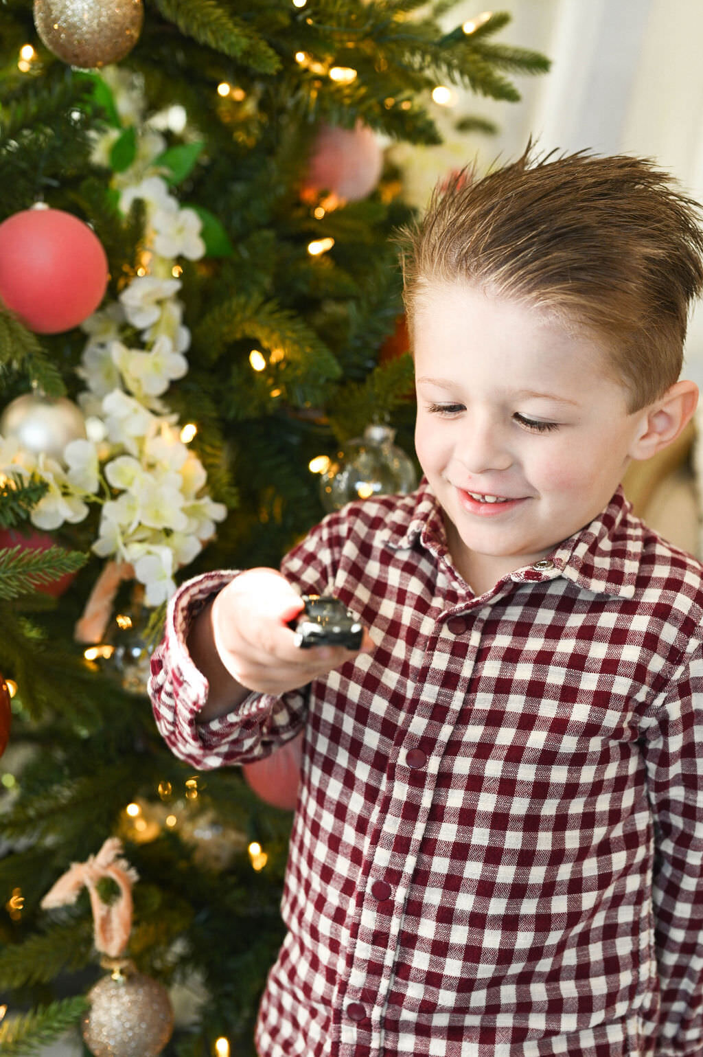 A small boy standing next to a Christmas tree holding up a toy car.
