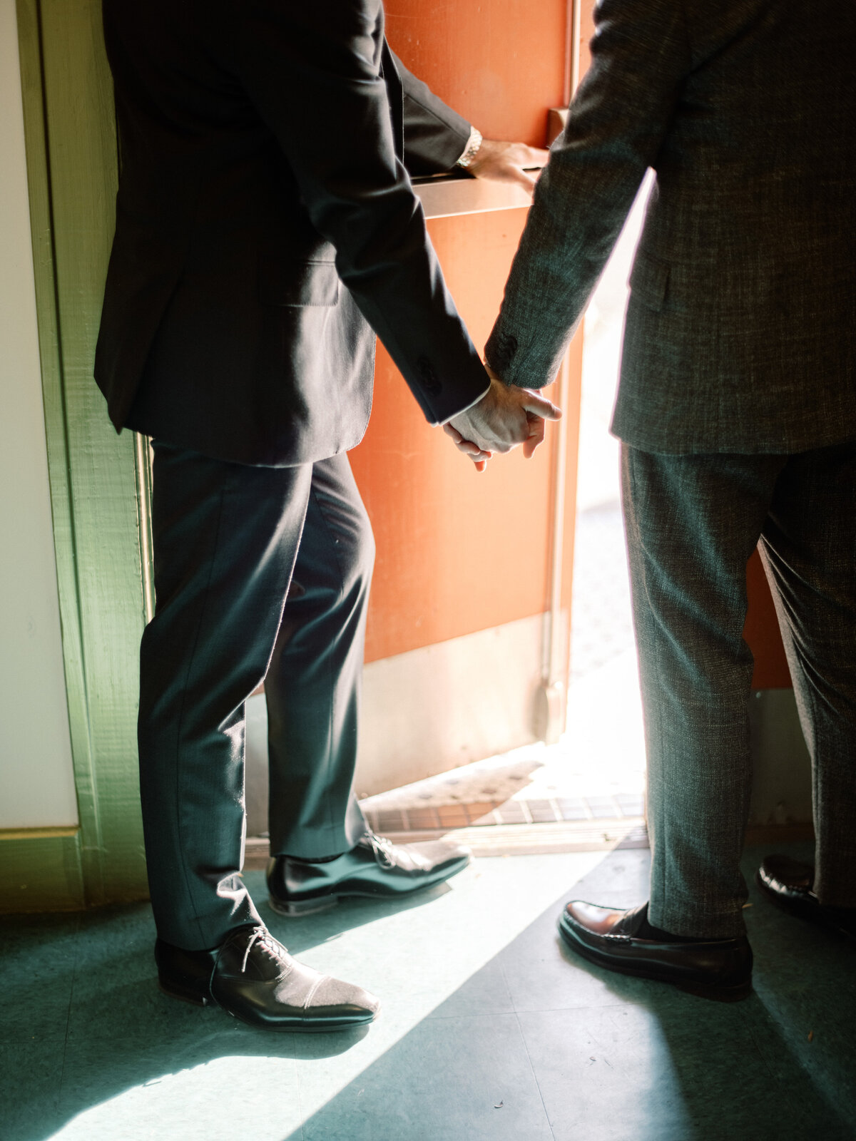 A romantic moment captured as two grooms share a tender hand-holding gesture right before the start of their wedding ceremony, symbolizing love and connection.