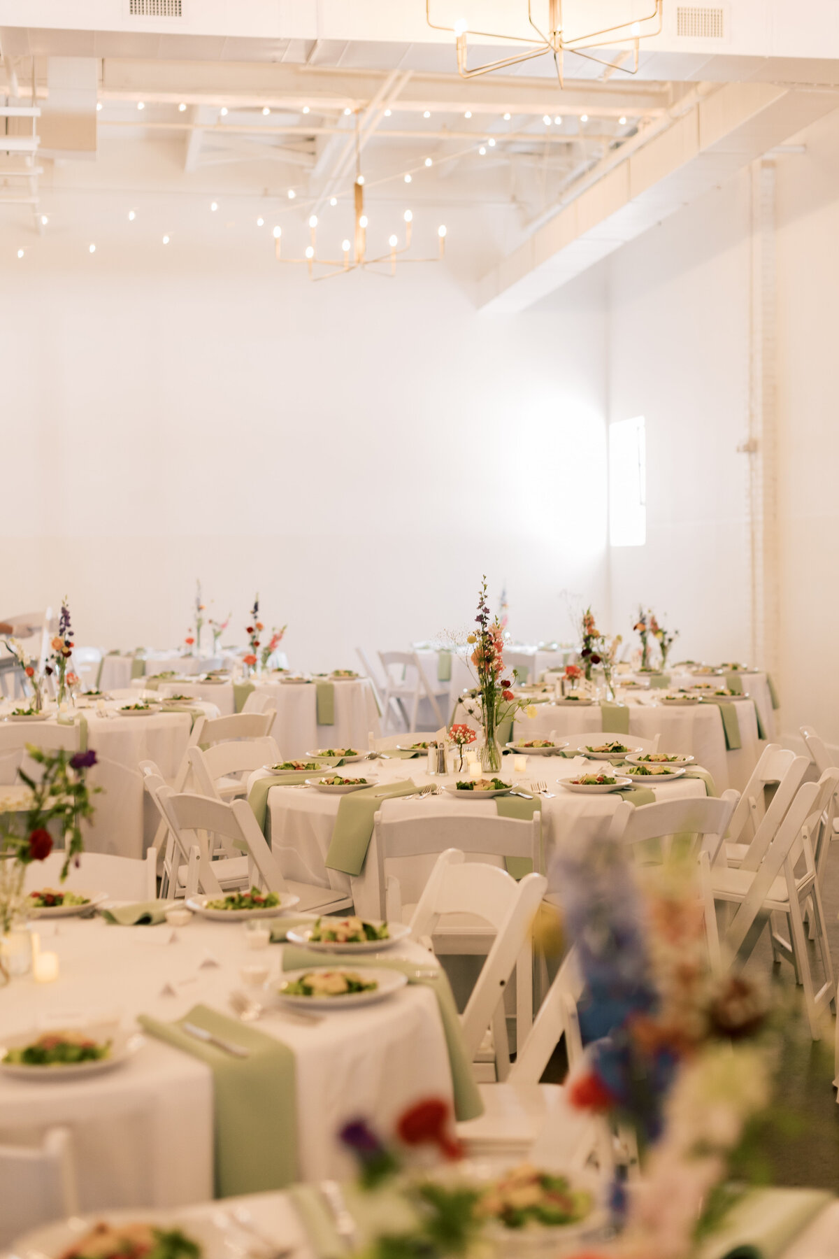 Sara and Brendan sitting at sweetheart table decorated with Crimson & Clover florals and candles during Fetewell reception.