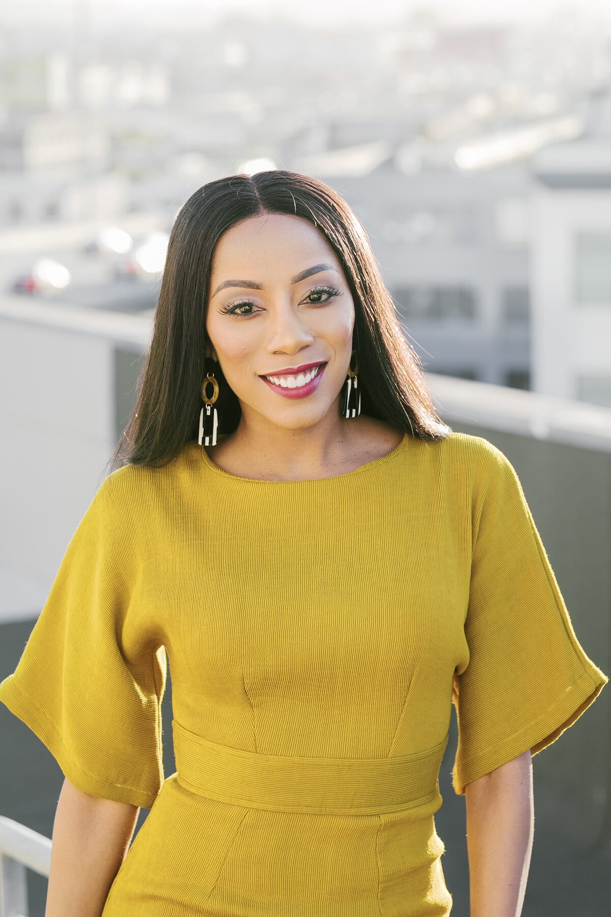 Black woman in yellow dress smiling in sunlight on rooftop deck during New York City brand shoot.