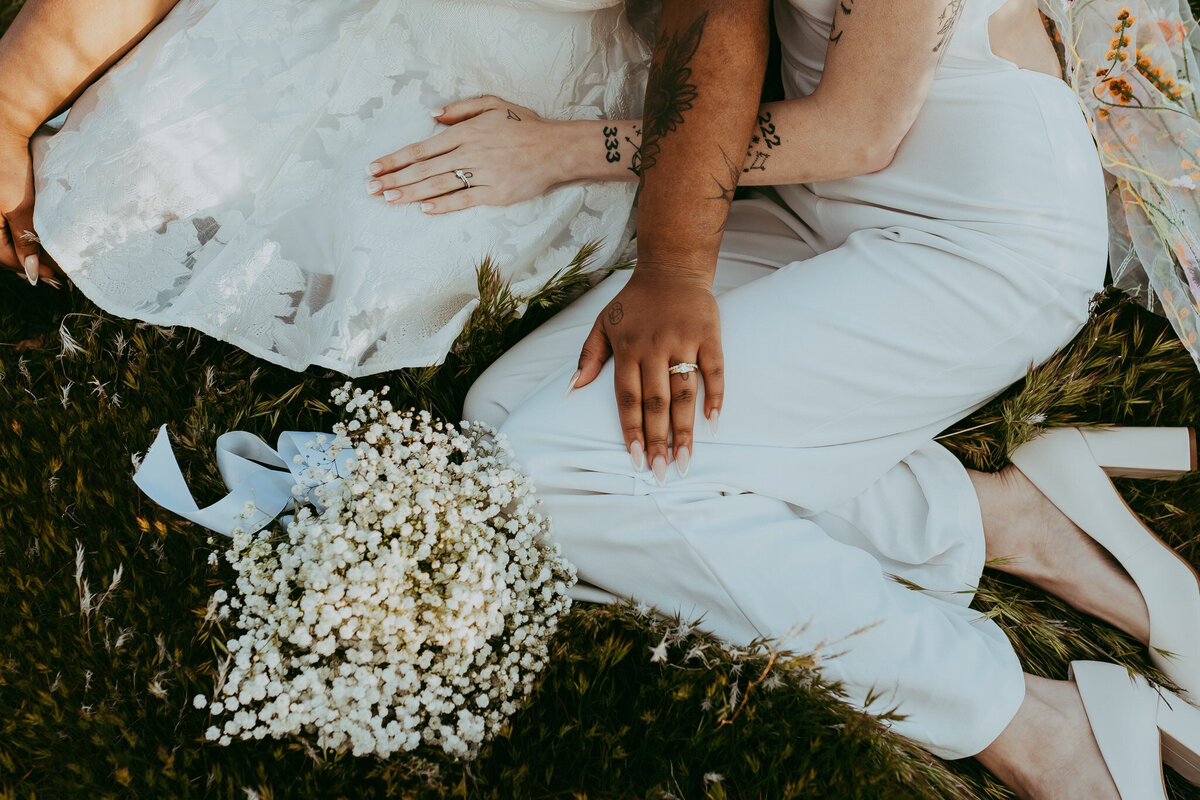 two brides sit together in lush grass