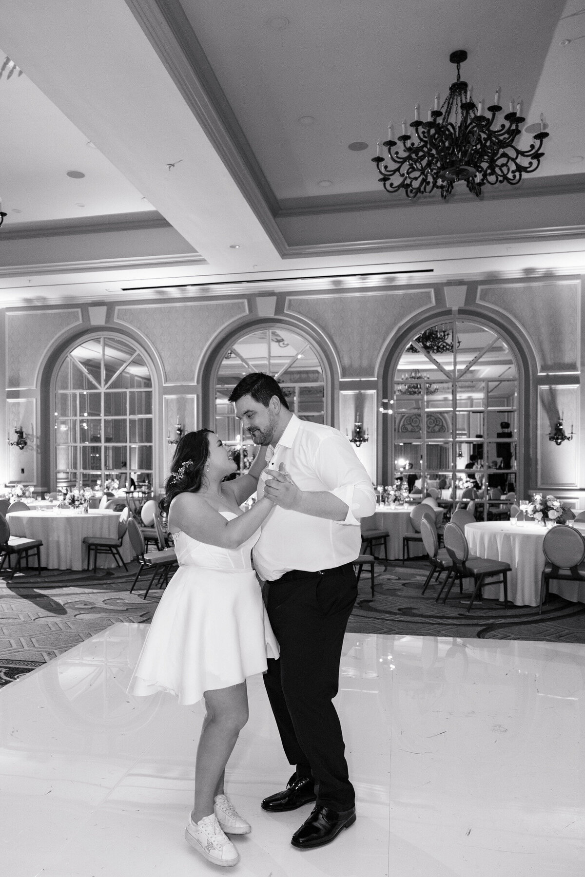 bride and groom during their last private dance elegantly styled wedding reception table at The Adolphus in Dallas featuring a black tablecloth, tall glass vases with pink rose arrangements, numerous candles, and refined glassware and chargers