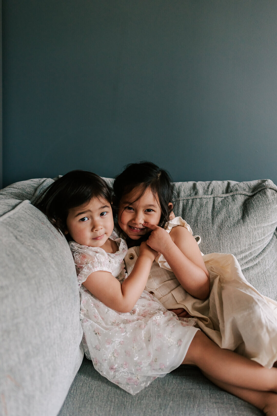 Two young sisters hugging each other on their sofa and having fun together
