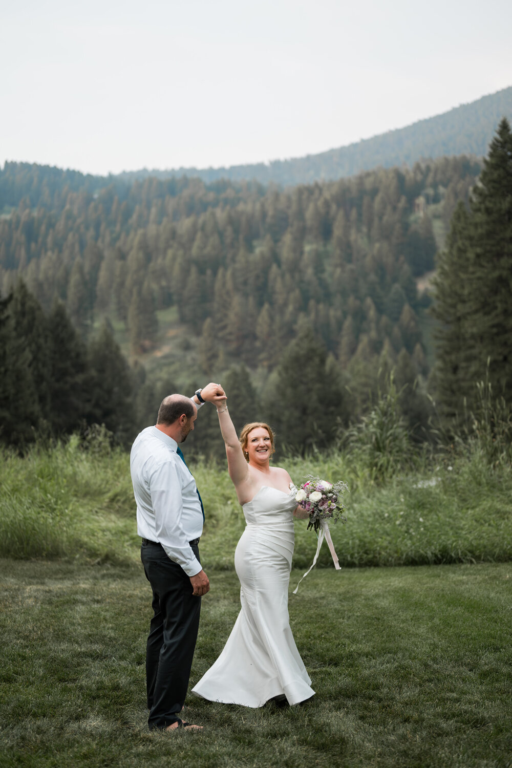 Groom twirling bride in a among greenery and majestic mountain backdrop during their Montana summer wedding at The Woodlands at Cottonwood Canyon.