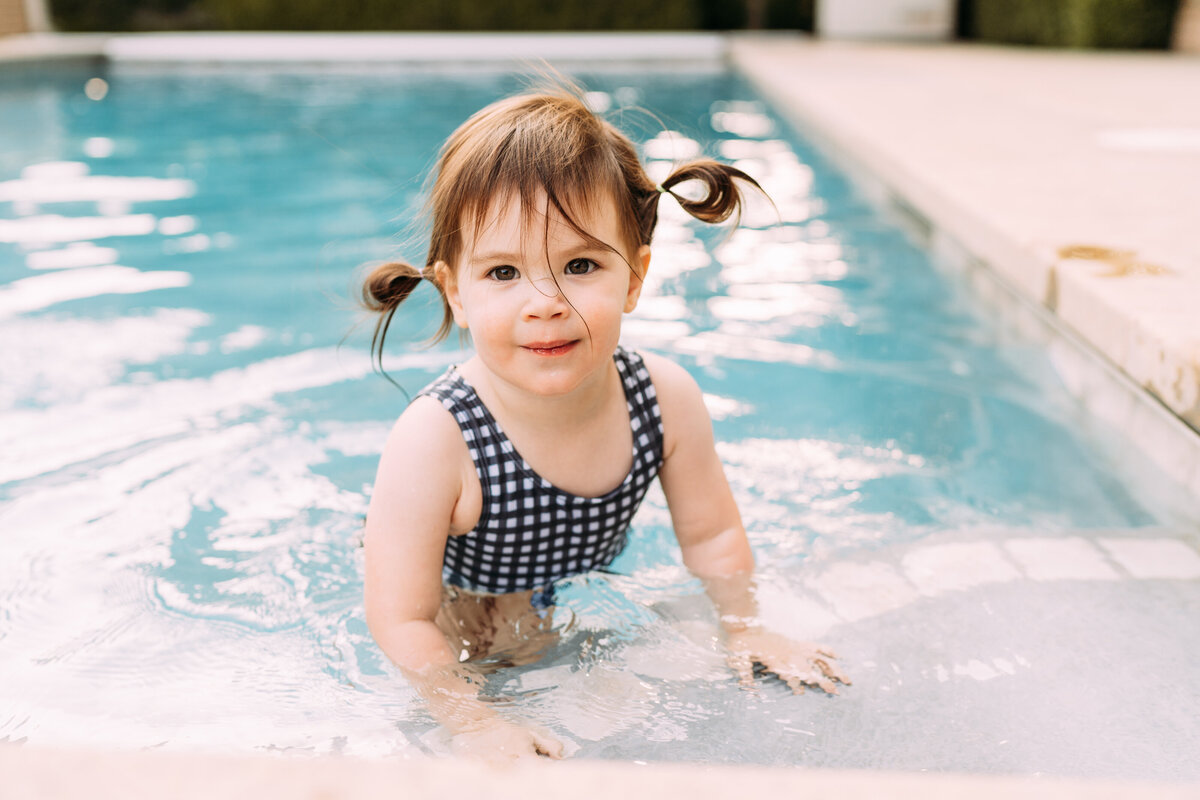 toddler girl swims in pool with pigtails