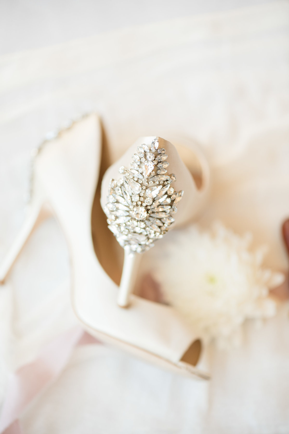 Bride's beige high heels with large diamond rhinestones on the back laying crisscross over each other.