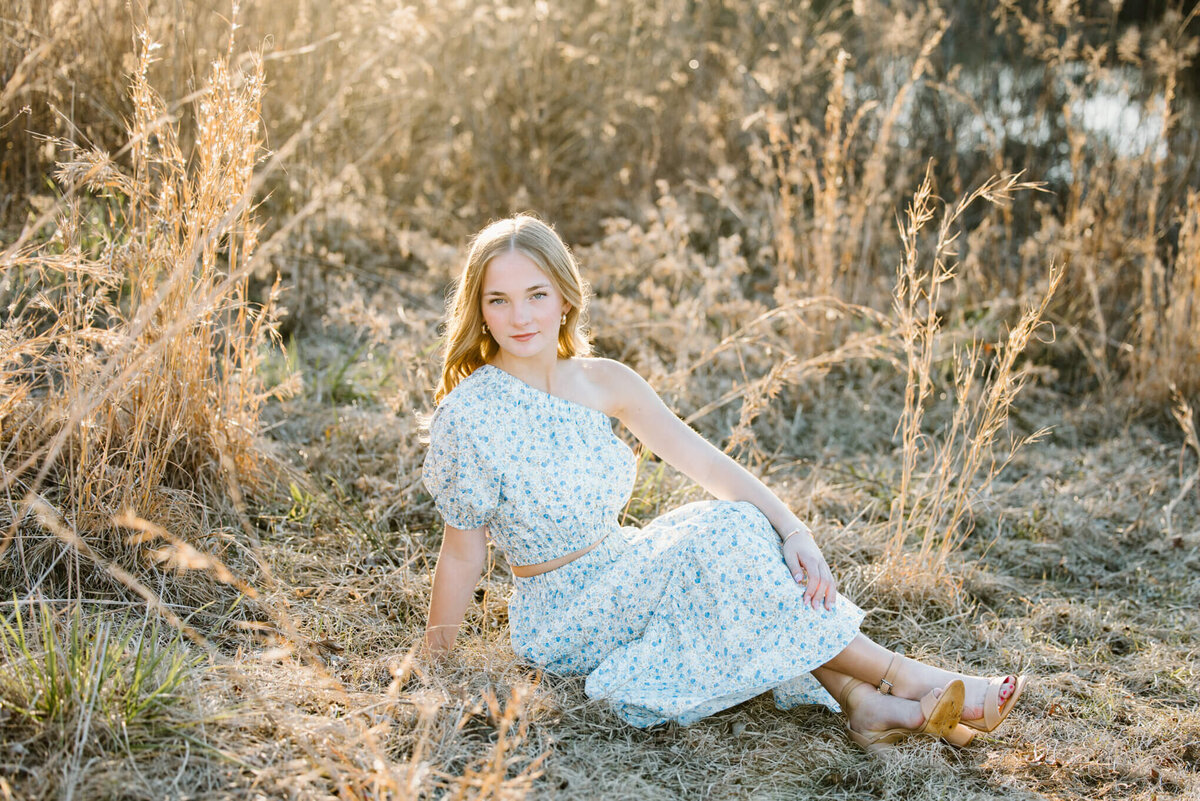 photograph of teenage girl in long dress sitting in open field during family photo session