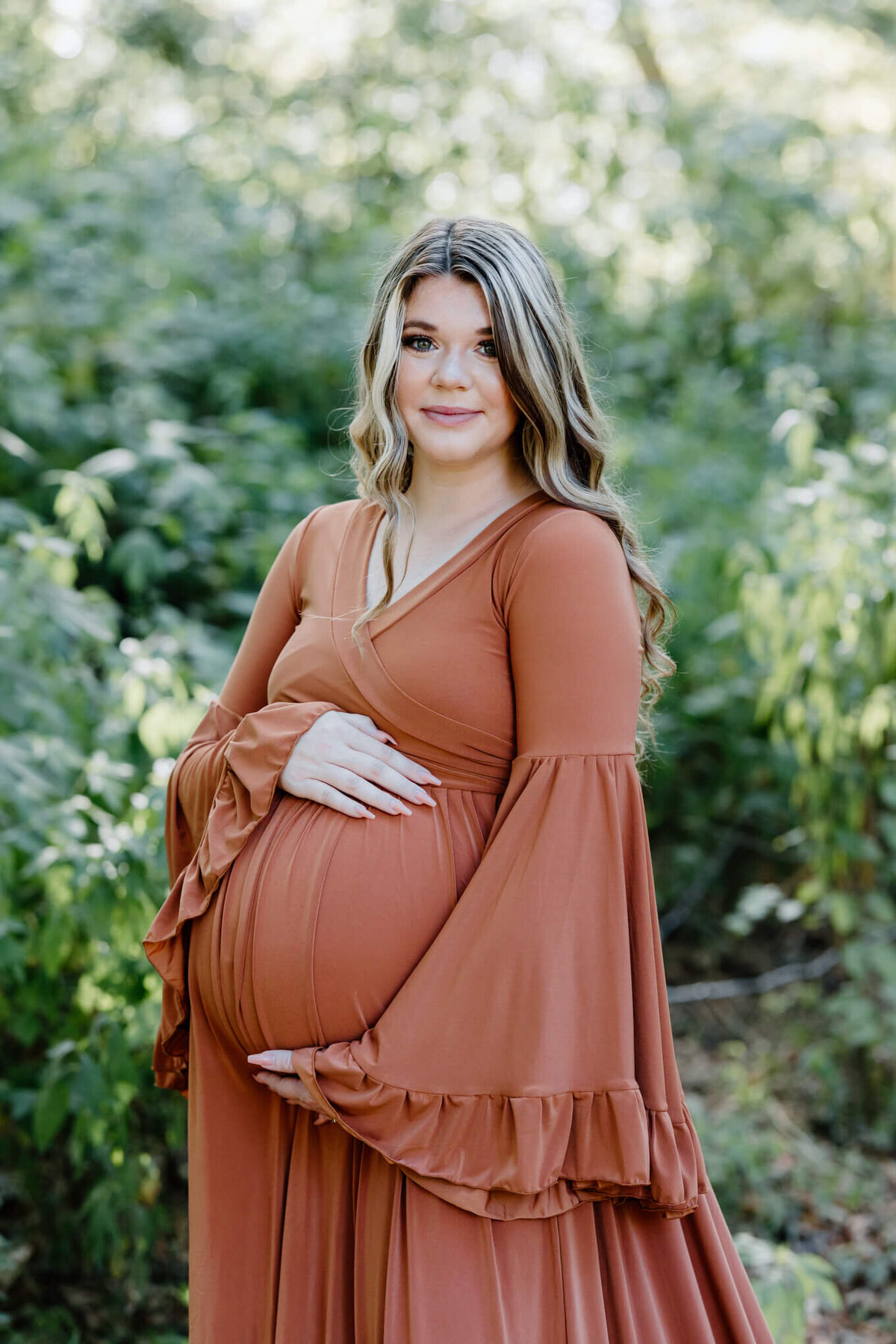 pregnant mother in dark orange maternity dress standing in an open field in Longview, TX