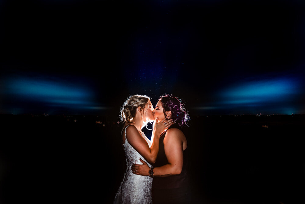 Two brides kissing in a dark space with blue light shining for romantic wedding photography by Maryland wedding photographer