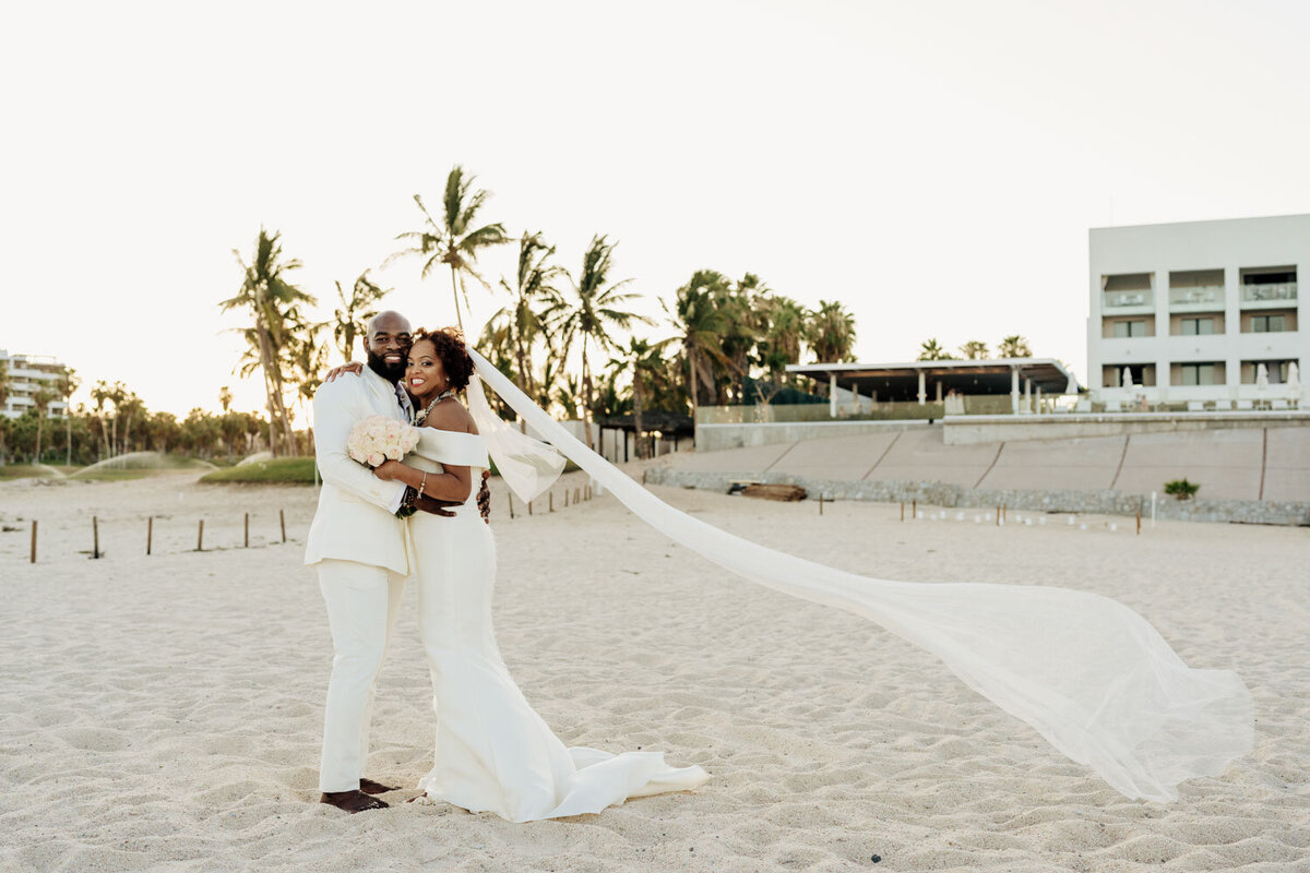 Bride and groom embracing on the beach with a long flowing veil