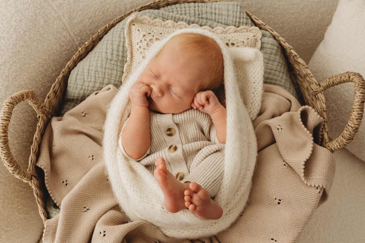 Ruua Hamdan Photography (UK): A newborn baby with red hair sleeps peacefully in a woven basket, wrapped in soft blankets.