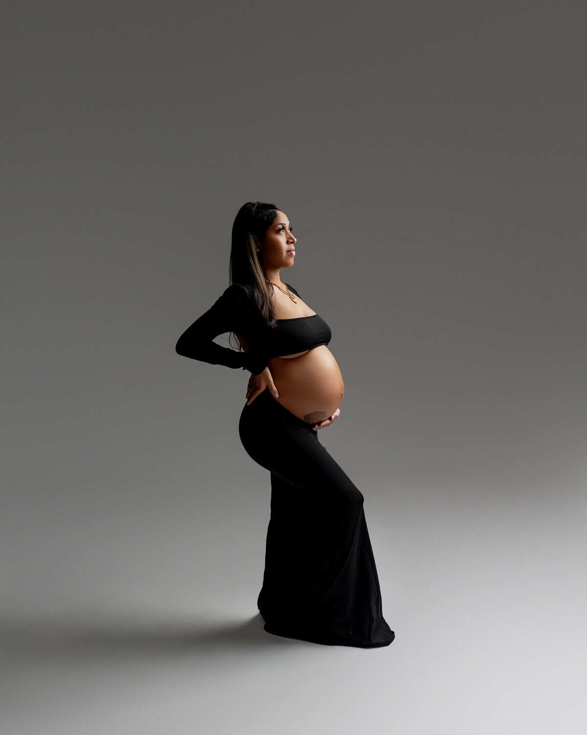Mama-to-be in a black dress, she poses in a side view, radiating grace and anticipation for her growing family. Captured by Inland Empire photographer Kaitlyn Dawn Photography.