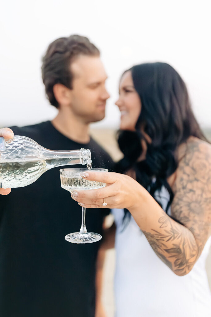 Romantic couple pours champagne during engagement session, captured by Lorissa Lee Photography. Featured on Brontë Bride.