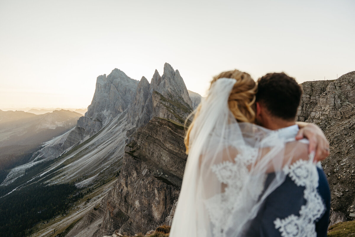 Bride and groom standing on cliff edge overlooking the Dolomites