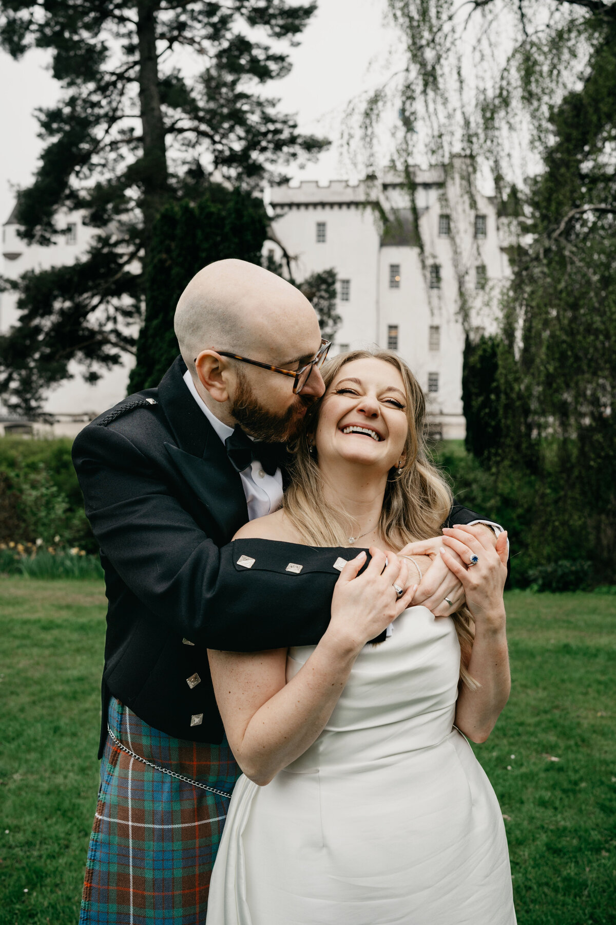 A newly married couple hug and kiss outside Blair Castle as their photographer takes wedding portraits.