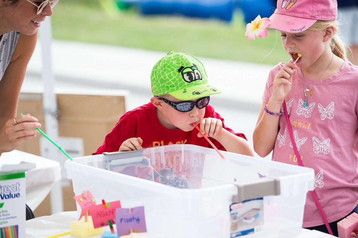 Ottawa event photography showing a little boy in a red t-shirt participating in fun straw blowing activity during a corporate children's event.  Captured by JEMMAN Photography COMMERCIAL