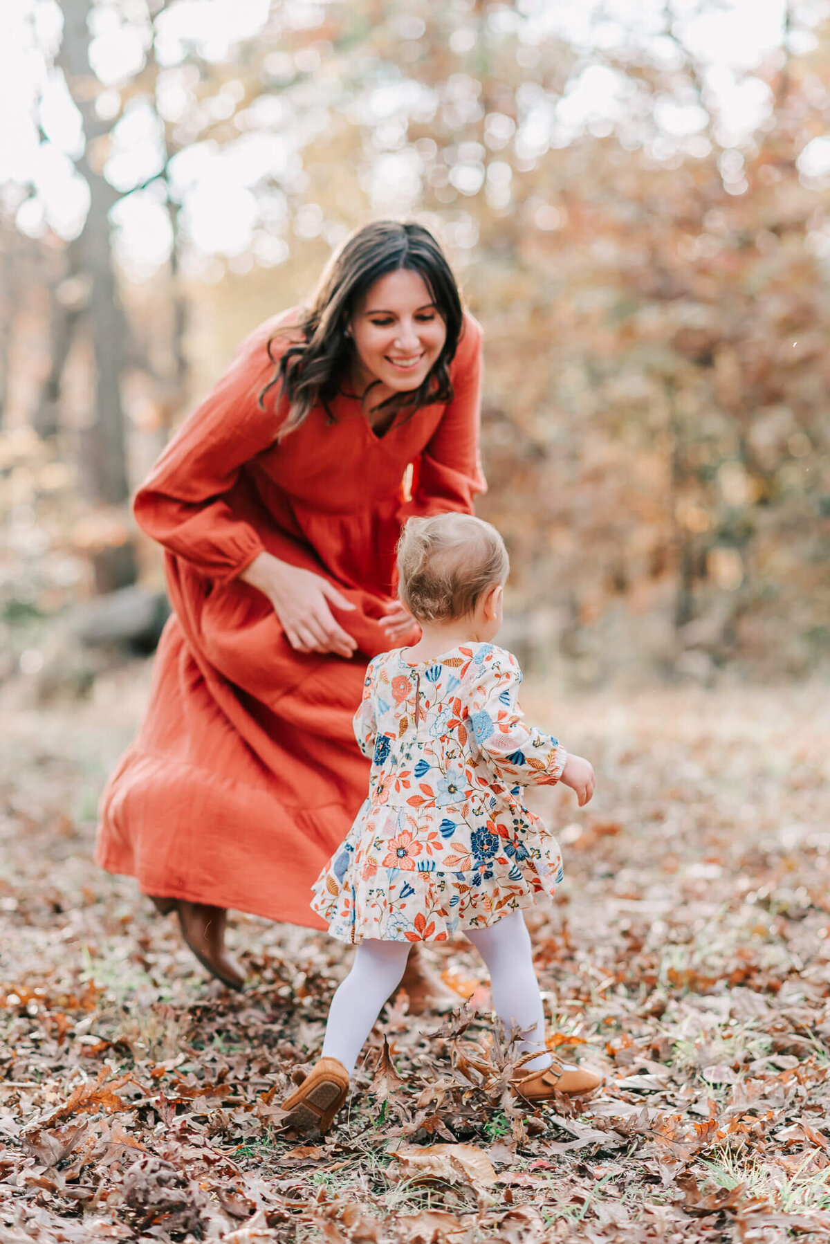A woman in a long orange dress chases after her daughter wearing a floral pattern