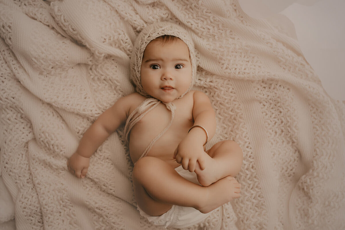a six month old girl holding her feet laying on her back on a cream set