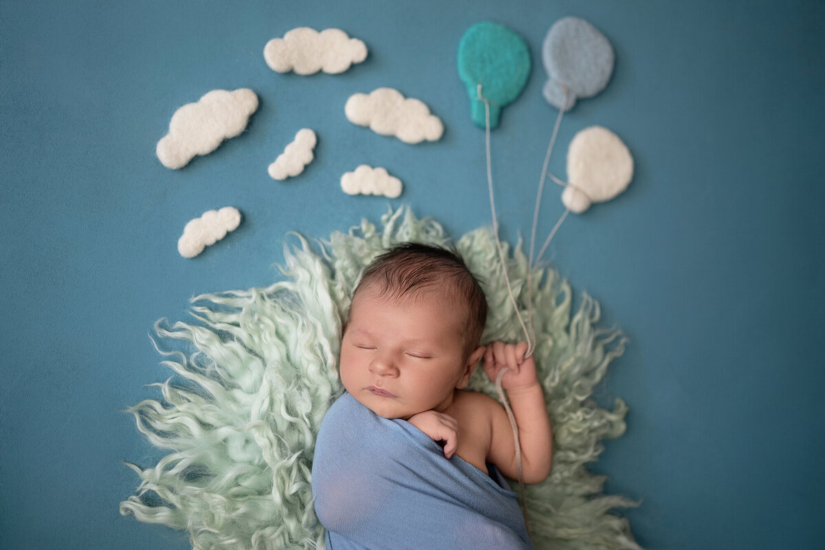 A newborn holds the string of felt balloons while sleeping in a studio