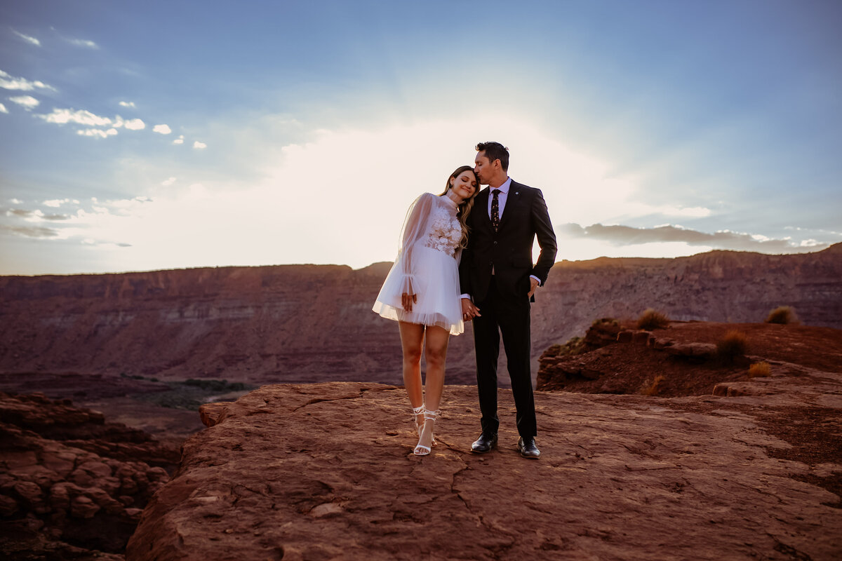A couple standing on a rocky cliff during sunset, holding hands with warm smiles, photographed by an Oregon Coast Elopement and Wedding Photographer.