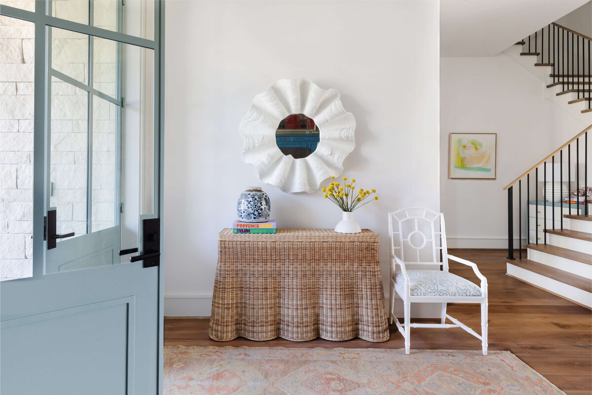 oyster creek studios memorial new build white accent mirror with wicker accent table and white chair in entryway