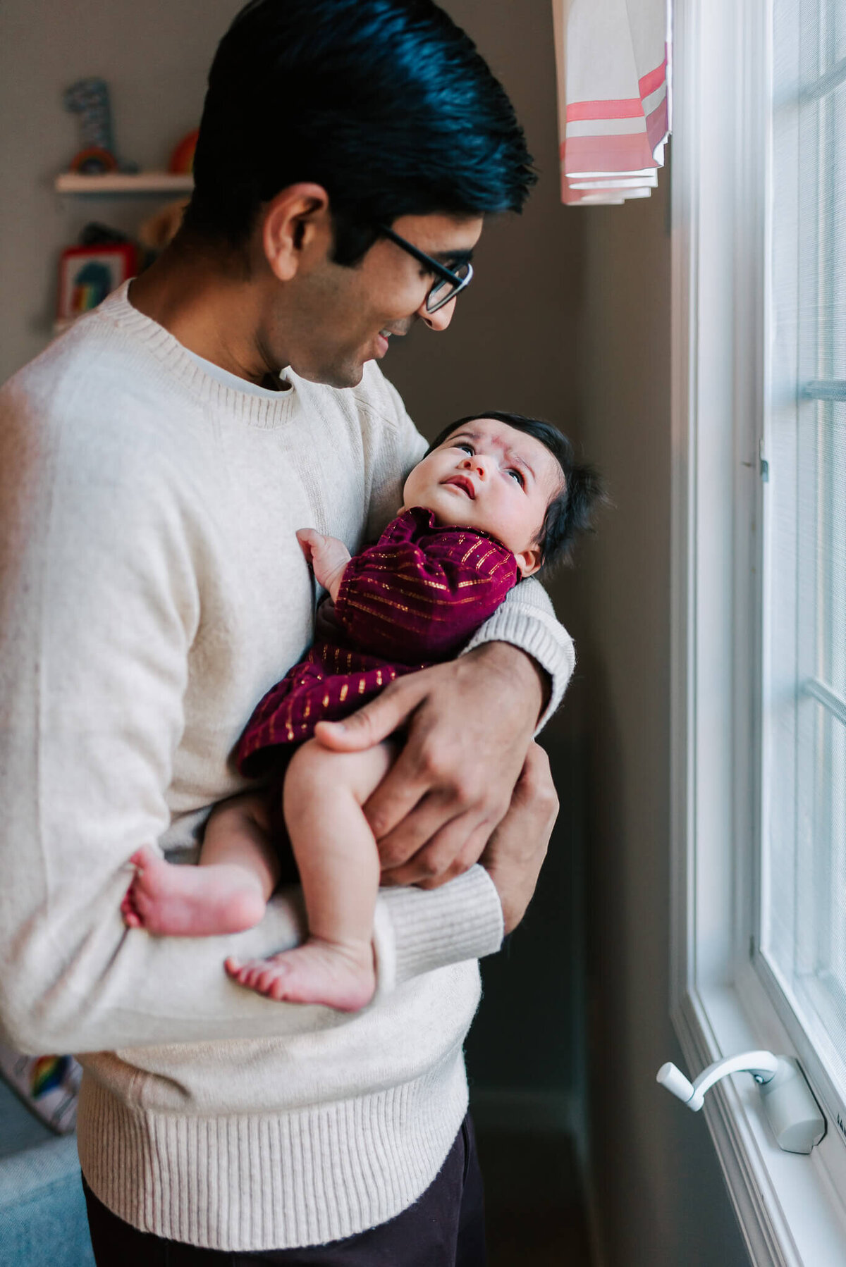 indian man holding and smiling at his newborn daughter in their northern VA home